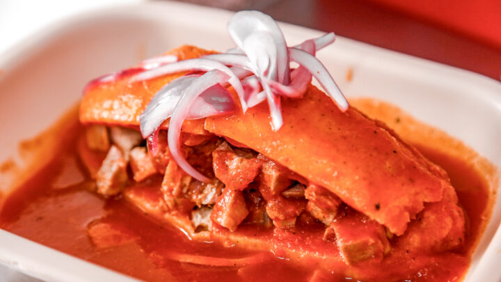 Torta ahogada de Guadalajara servida con salsa de jitomate, carnitas, cebolla encurtida y limón.